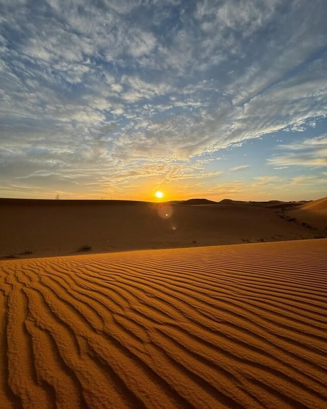 Rippled sand dunes at sunset under a wide sky